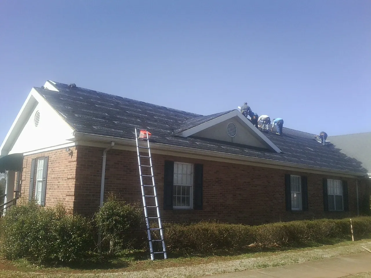 Crew tearing shingles off a brick ranch roof with a ladder set — Metal Roof Repair work by our crew in New Lenox