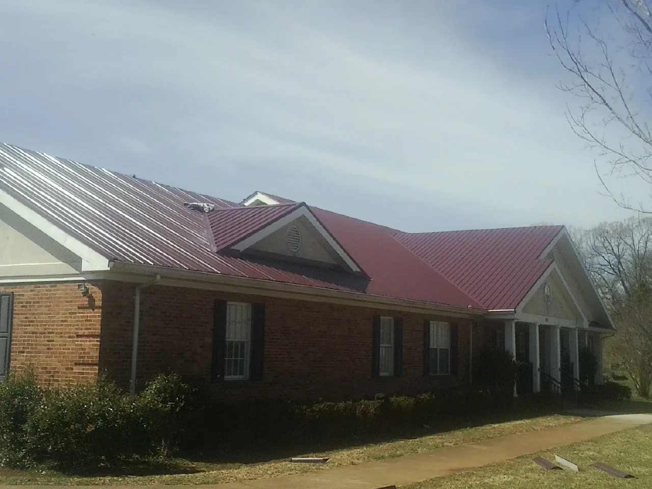 Red metal roof with gabled entries on a long brick building, from a Hail Damage Roof Repair job in New Lenox