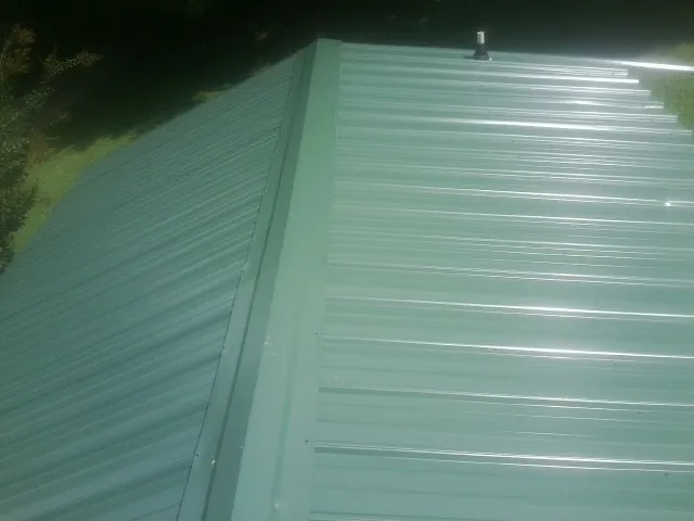 New green metal panels meeting at the ridge of a roof — Flat Roof Repair work by our crew in New Lenox