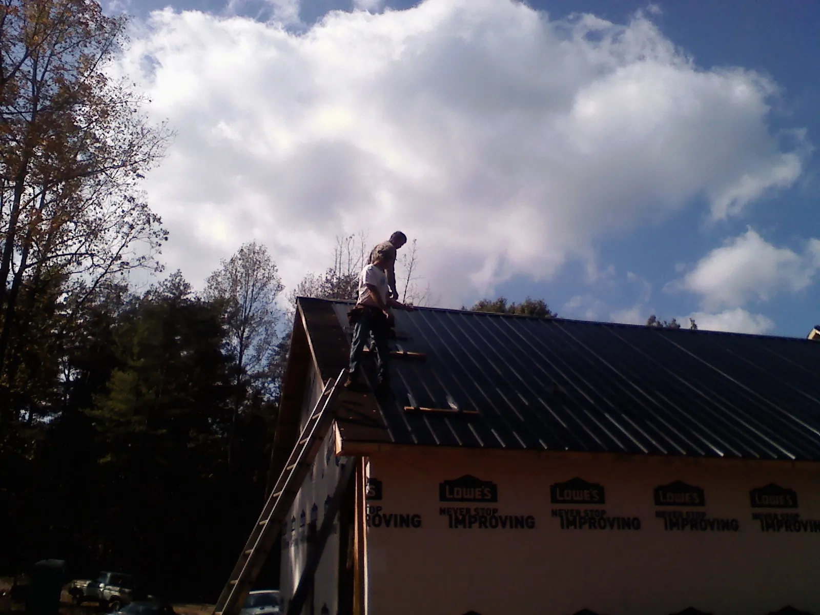 Roofer fastening dark metal panels high against a cloudy sky, from a Roof Inspection job in New Lenox