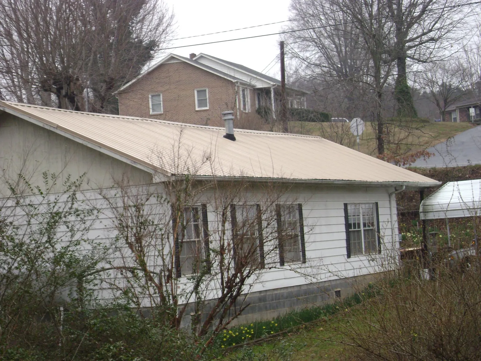 Tan metal roof on a white sided house set into a hillside — Commercial Roofing by Roofing Brothers in New Lenox